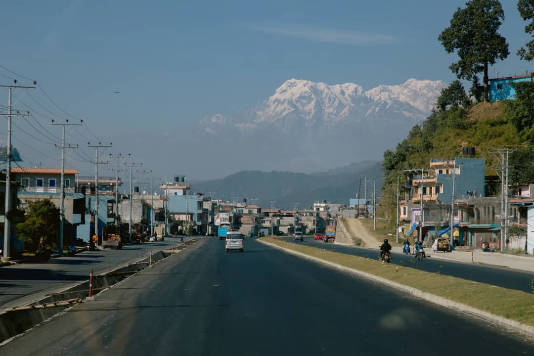 A tranquil view of a road leading to the Himalayas with snow-capped peaks in the background.