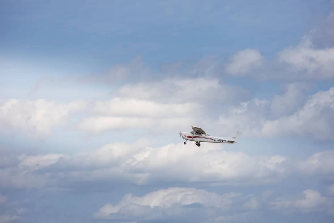 A small aircraft navigating through a bright sky, surrounded by fluffy clouds.