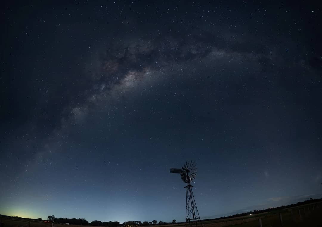 A breathtaking view of the Milky Way stretching over a silhouetted windmill in Rodgers Creek, QLD, Australia.
