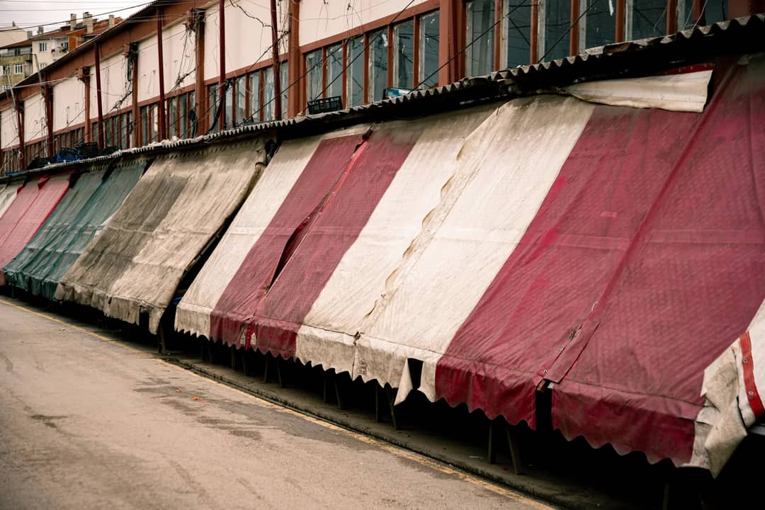 Row of closed market stalls with colorful striped awnings in an empty street.