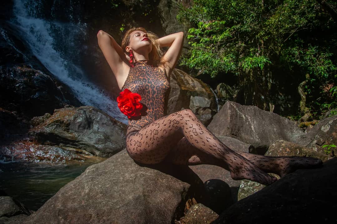A woman in a leopard print outfit poses confidently by a waterfall, surrounded by nature.