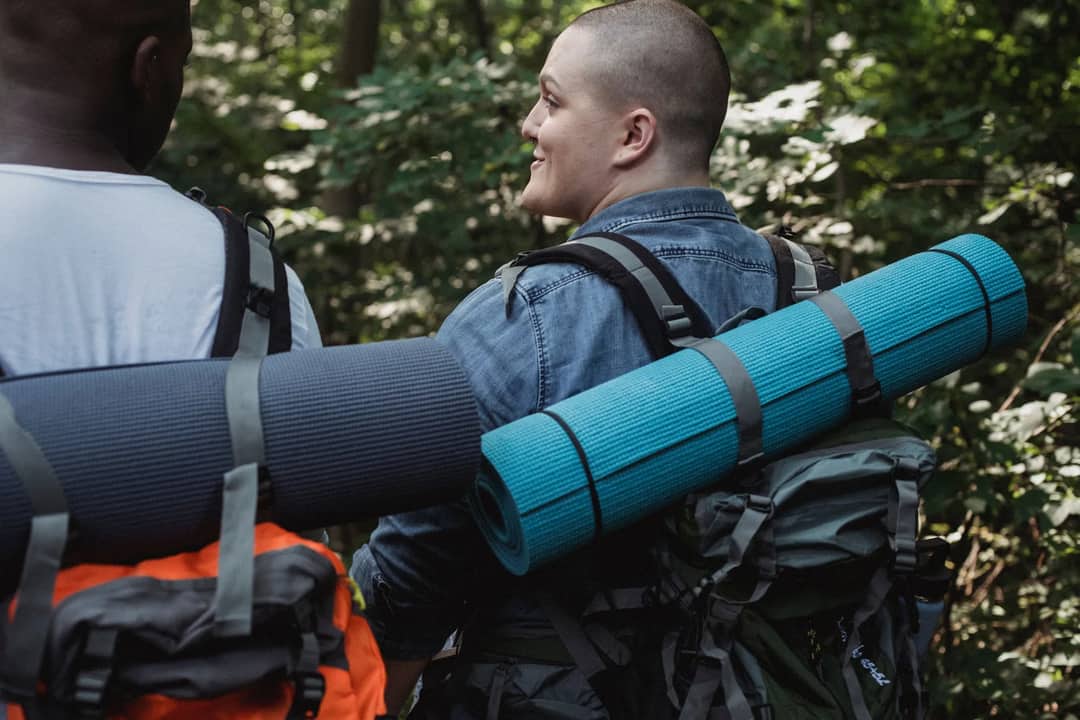 Back view of multiracial friends in casual clothes carrying backpacks with hiking equipment trekking in nature in daylight