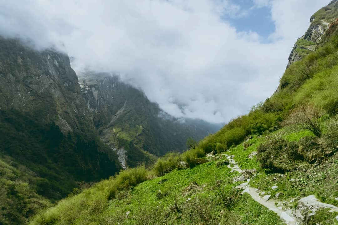 Explore a scenic mountain path enveloped by lush greenery and towering cliffs in this summer landscape.