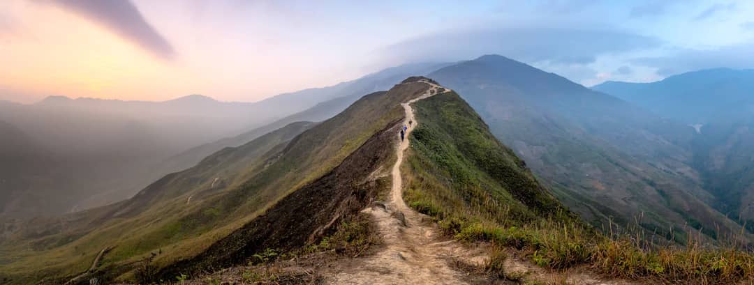 Group of travelers walking on path on grassy top of mountain ridge located in mountainous valley in mist