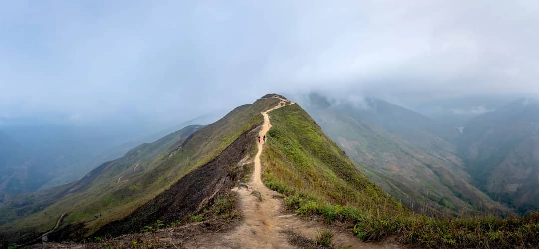 Wide angle of hikers strolling on top of grassy mountain while discovering mountainous terrain in mist