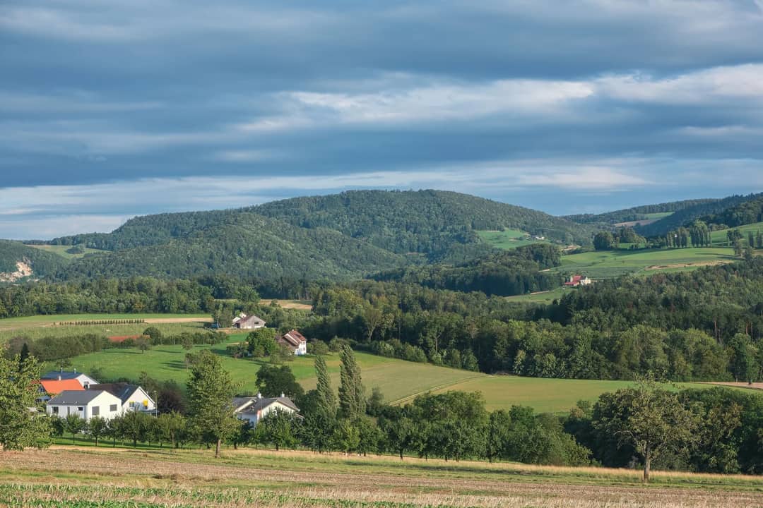 Beautiful rural landscape with fields, trees, villages, and rolling hills under a cloudy sky.