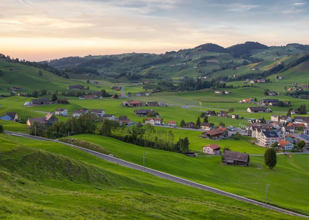 Idyllic Swiss village landscape with green hills and sunset sky, perfect for travel inspiration.