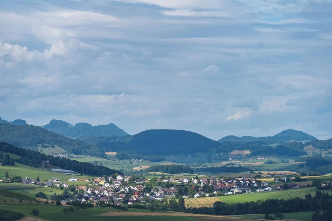 Picturesque rural village set against rolling hills and a vibrant countryside under a dramatic sky.