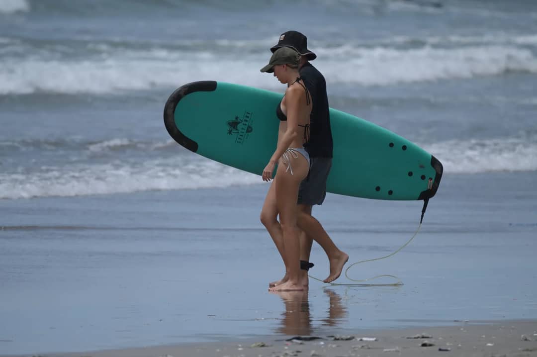 A couple walks along the sandy beach with a surfboard in Bali, Indonesia, capturing beach vibes and adventure.