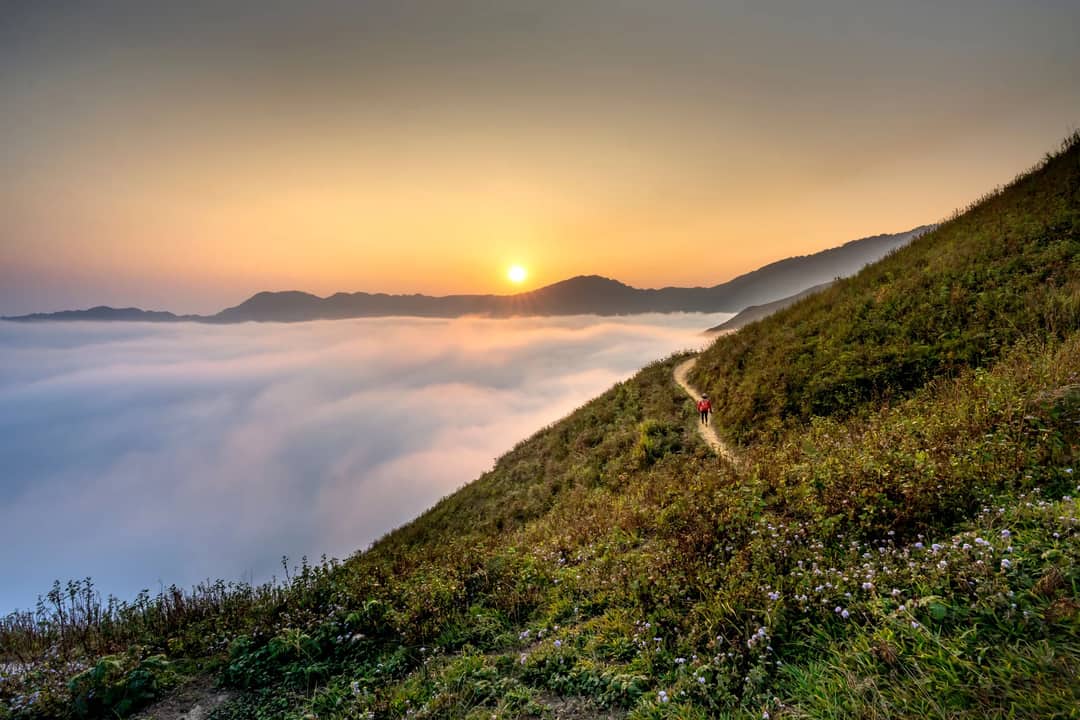 Stunning sunrise over a mist-covered mountain range with lush greenery and a solo hiker.