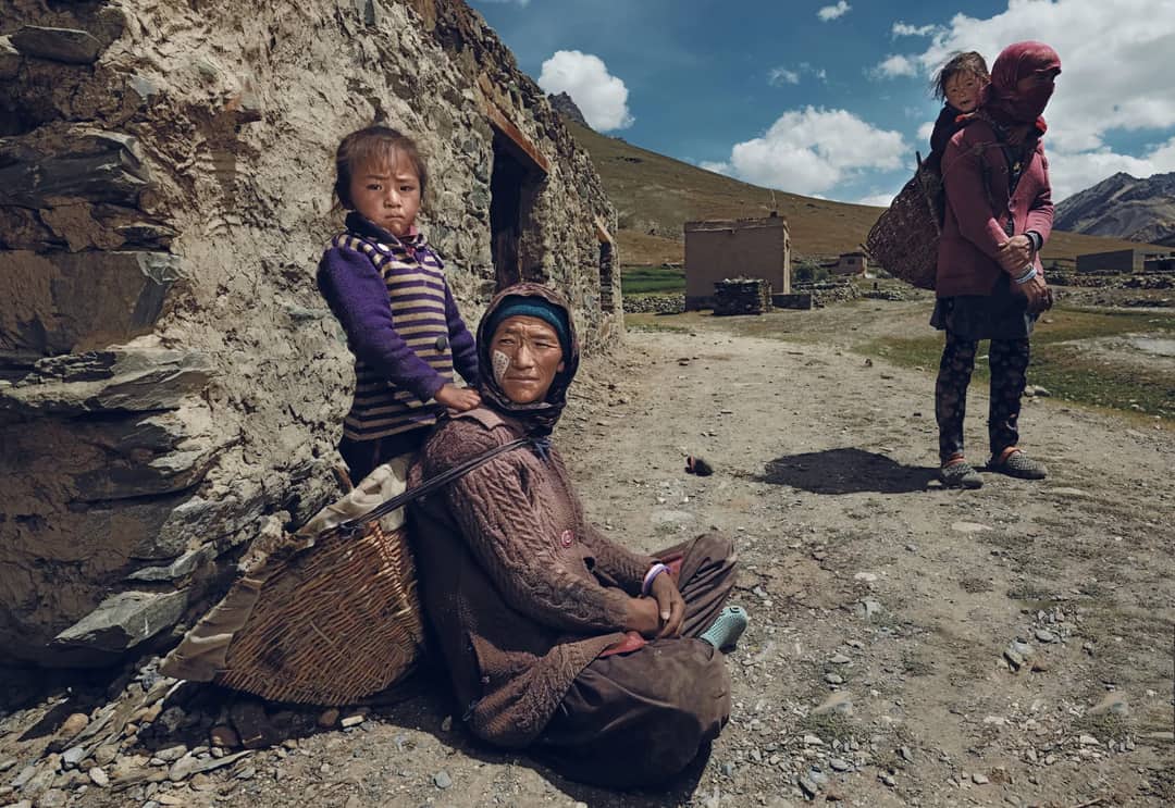 A rural family sitting and standing near stone buildings on a sunny day.
