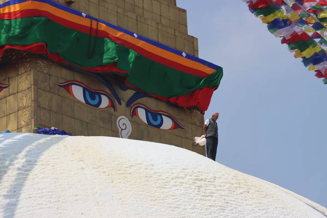 Boudhanath Stupa in Kathmandu with colorful prayer flags and a person walking on its dome.