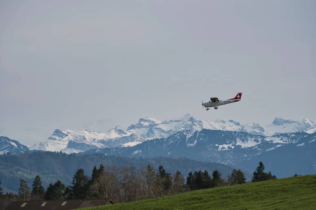 Light aircraft flying over snowy Swiss Alps with scenic landscape below.