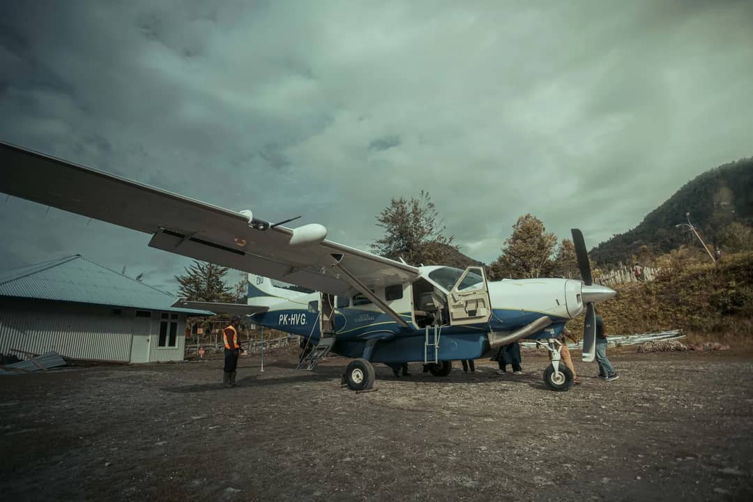 A small aircraft on a rural airstrip in Papua, Indonesia, surrounded by rugged terrain and lush greenery.