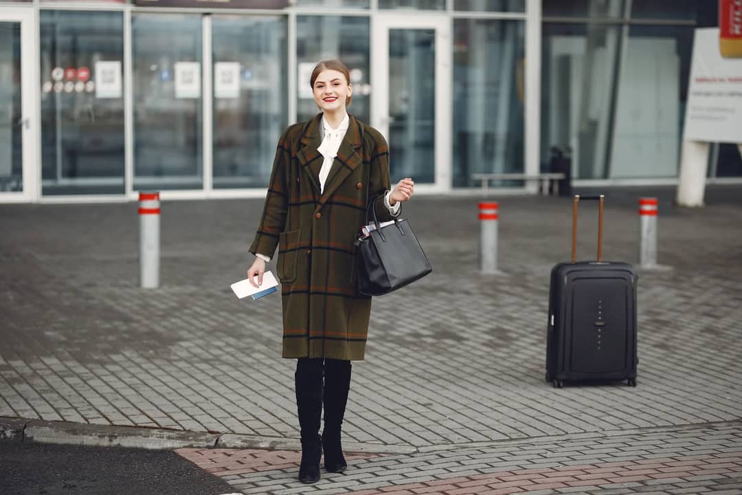 Fashionable woman with luggage arrives at airport ready for travel.