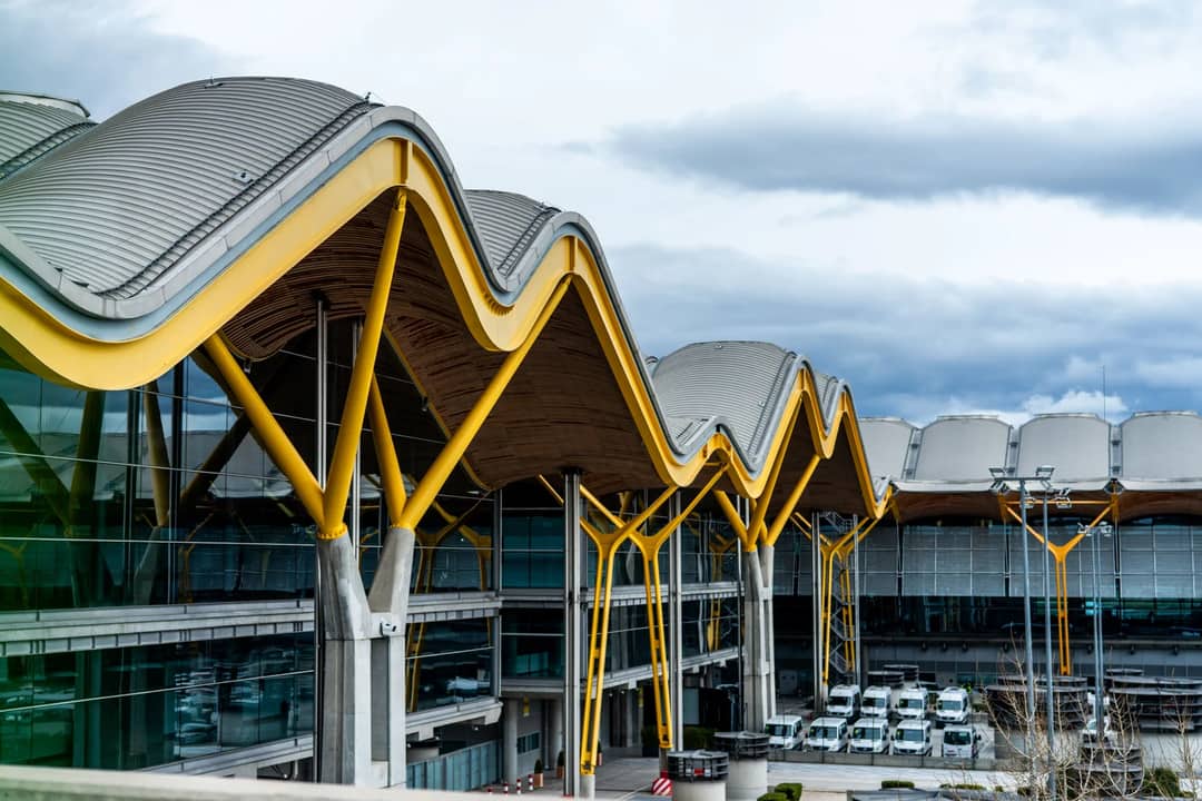 A striking view of a modern airport terminal with a distinctive wavy roof design and vibrant yellow supports.