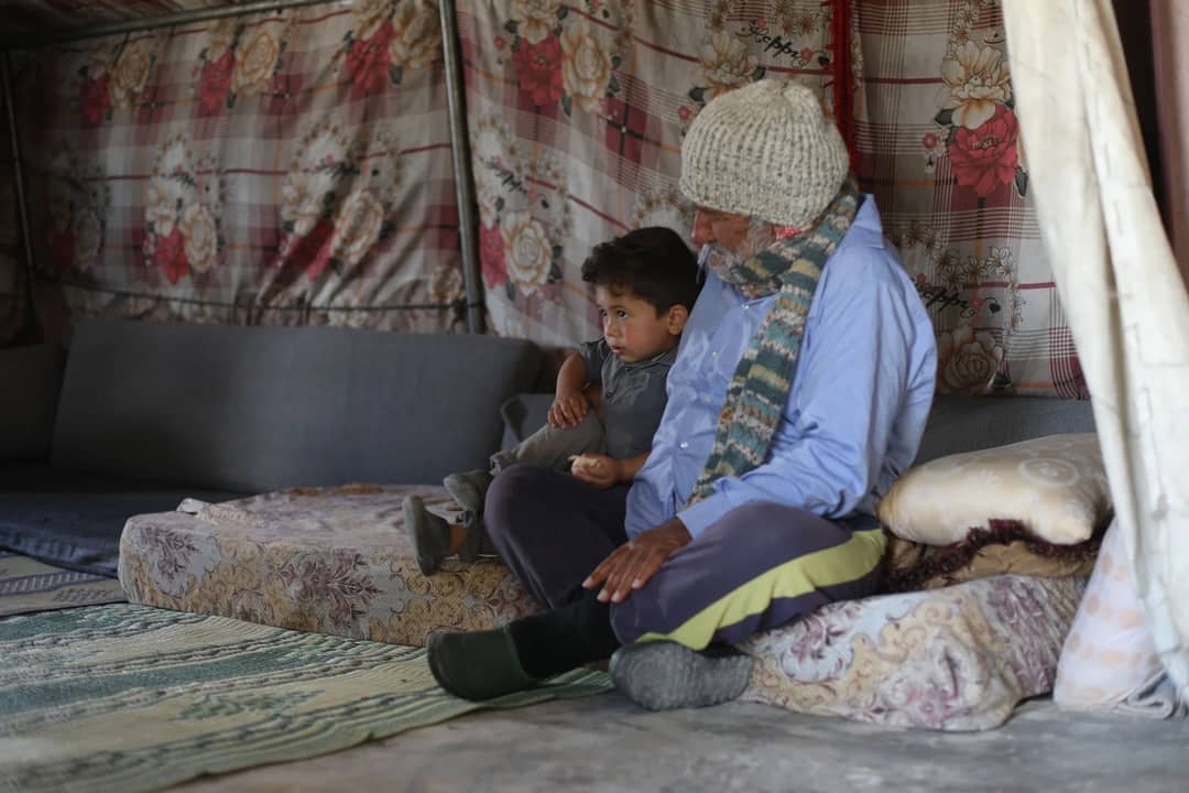 Older man and young boy sitting indoors, sharing a quiet moment. Cozy, warm atmosphere.