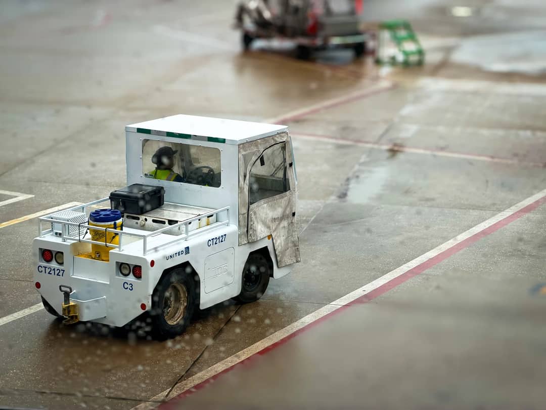 A small airport utility vehicle on a rainy tarmac, highlighting ground support operations.