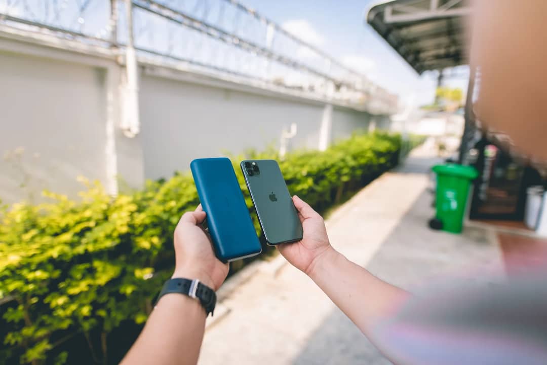 Close-up of a smartphone and power bank held in hands in an outdoor setting.