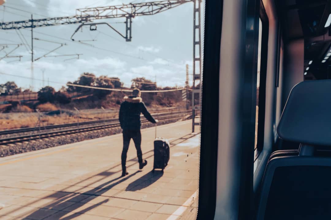 A man walks on a train platform with luggage, viewed from a train window.