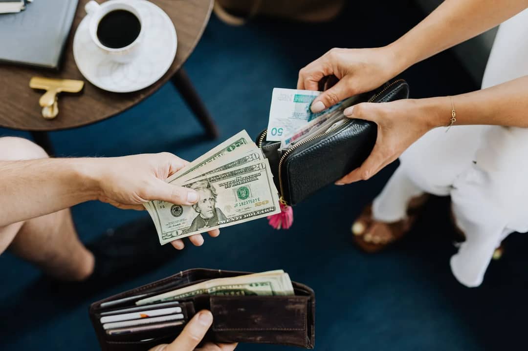 Cash banknotes of several currencies fanned out beside credit and debit cards and a wallet — the choice of how to carry and spend money abroad