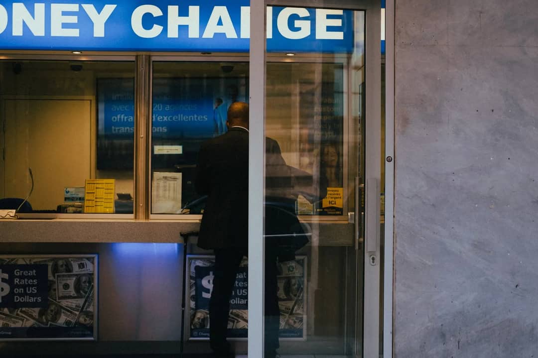 A currency exchange bureau counter with a foreign-exchange rates board and bundles of banknotes in different currencies