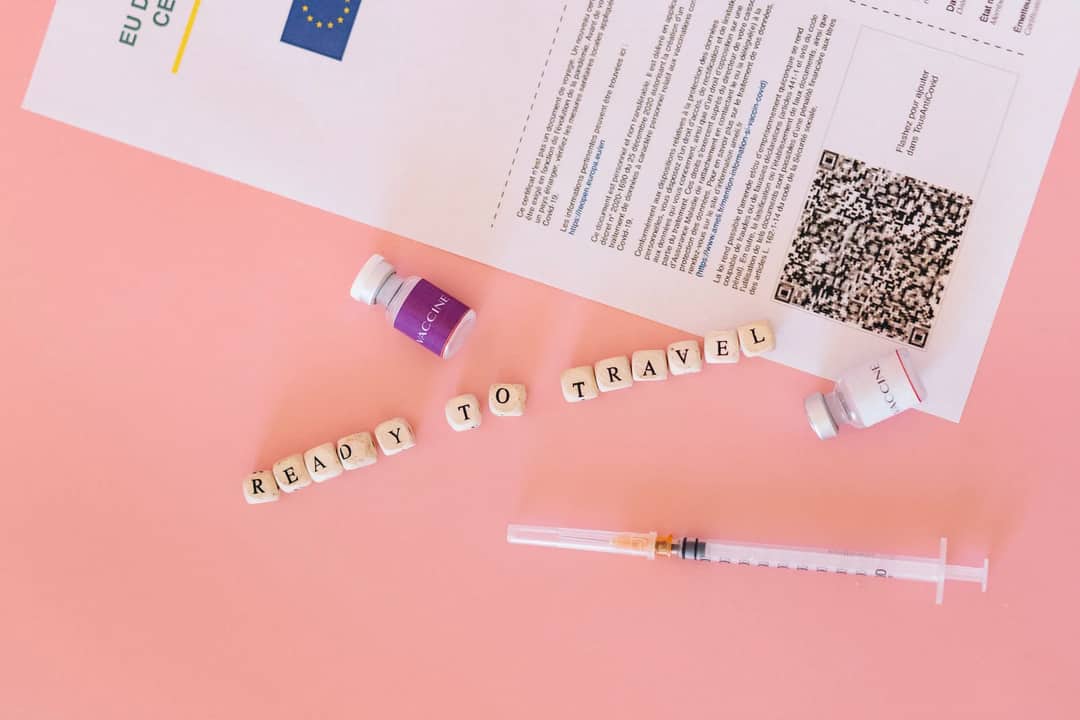 COVID-19 vaccine certificate with vials and syringe on pink background, ready to travel concept.