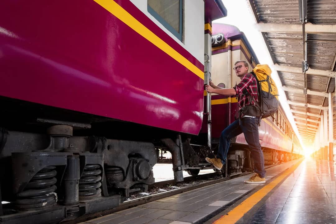 Man with backpack boarding a train at urban railway station during daytime travel adventure.