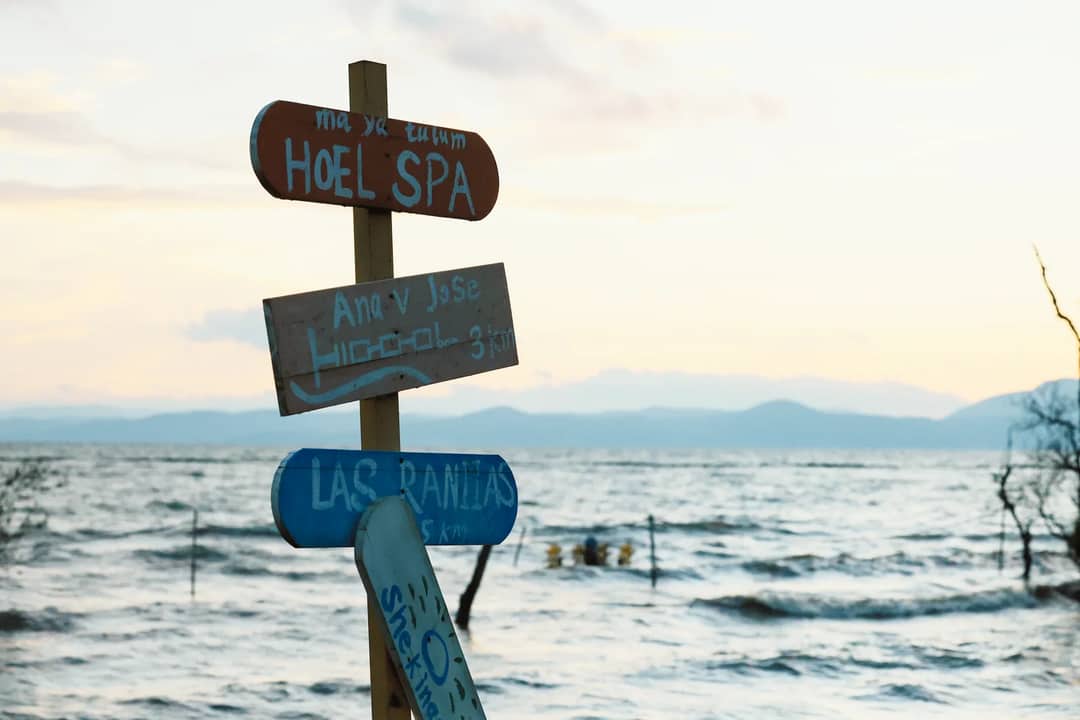 Wooden signposts by the sea during sunset, offering directions to local destinations.