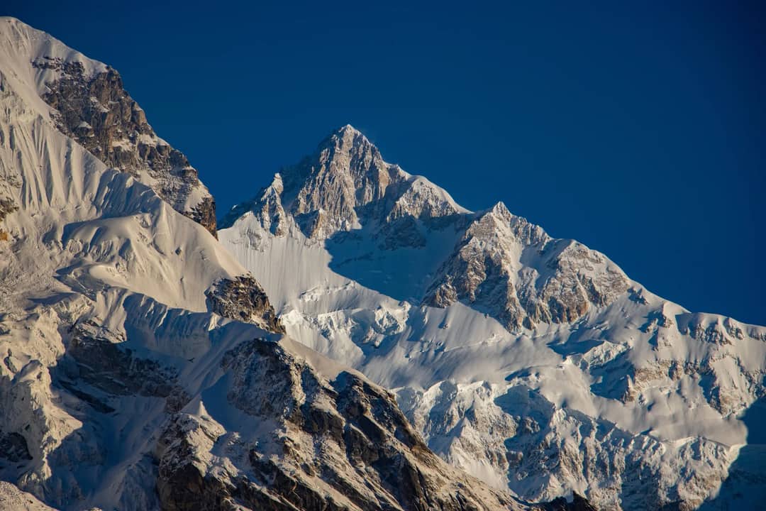 Snow-covered peaks of Kanchenjunga in Sikkim, India under a clear blue sky.