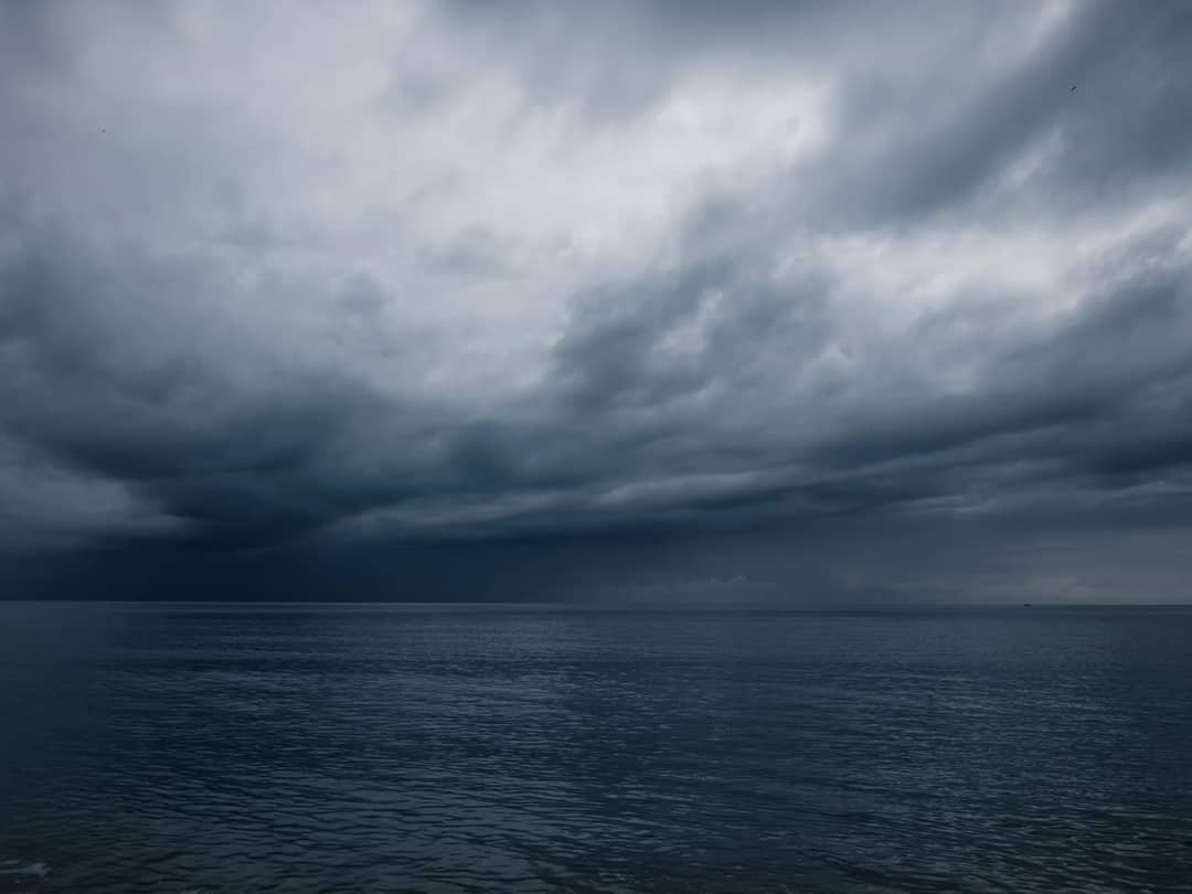 A dramatic seascape with dark clouds over a calm ocean at dusk, evoking a moody atmosphere.