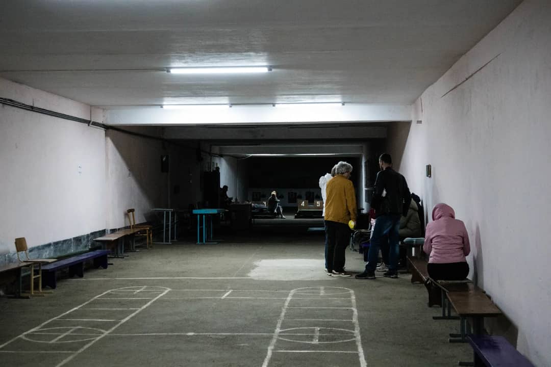 A group of people sitting and standing in an underground shelter with simple lighting and chalk drawings on the floor.