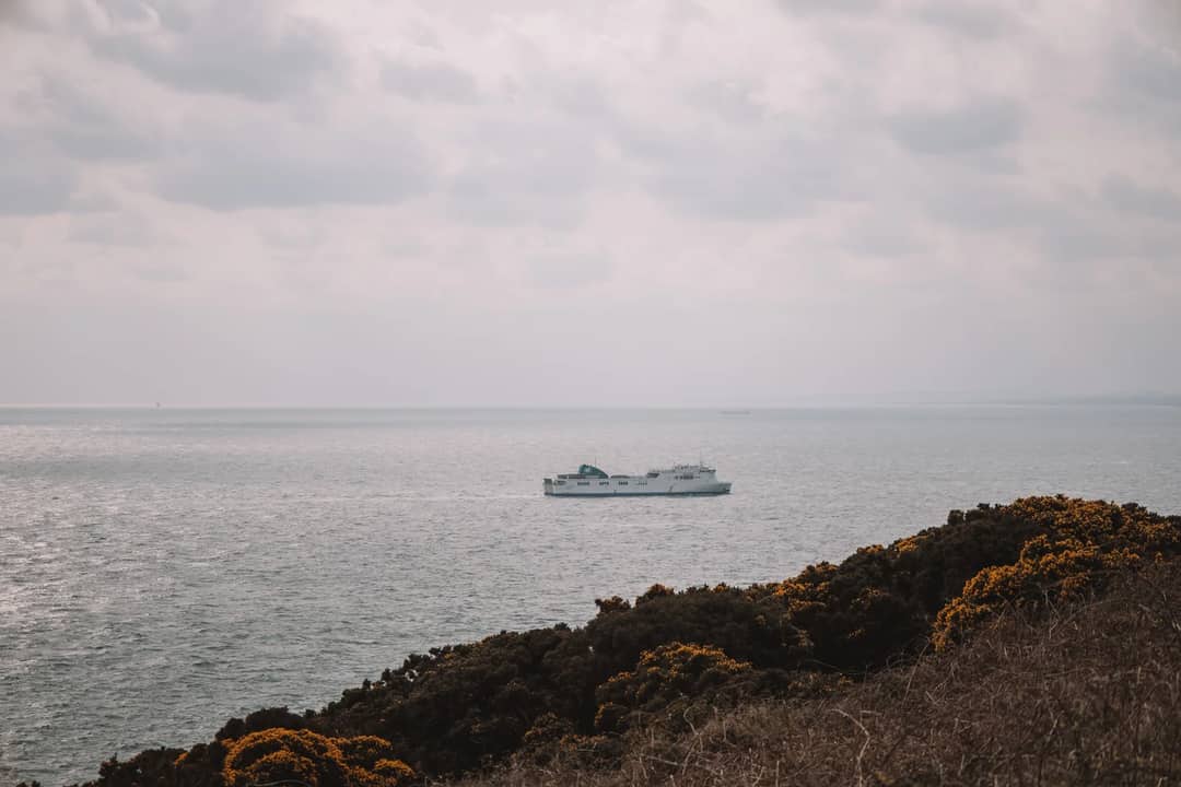 A ferry travels on Dublin Bay with a scenic view of the coastline under cloudy skies.