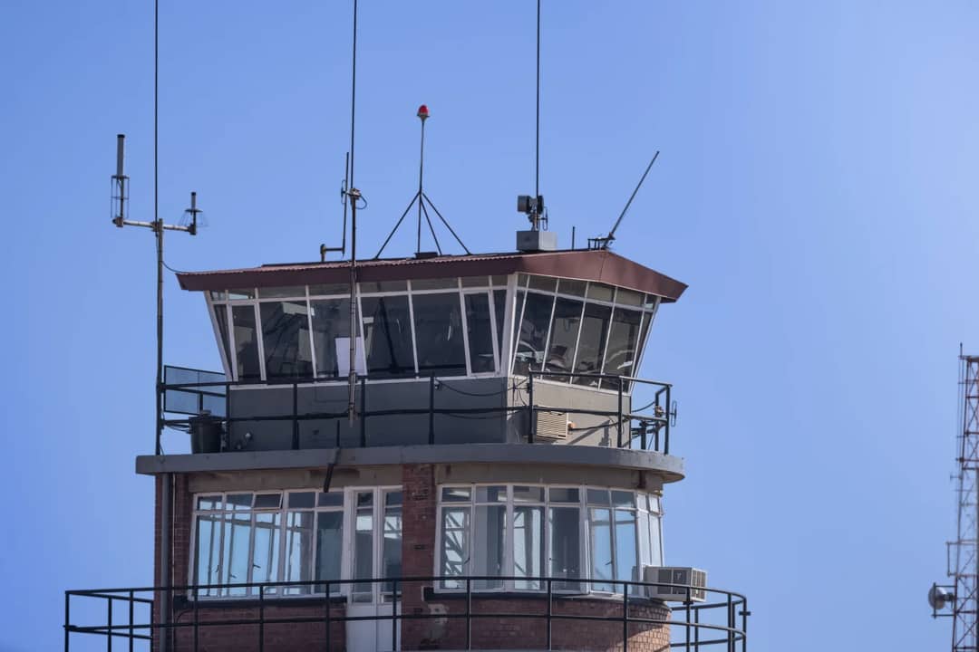 A modern airport control tower against a clear blue sky, showcasing aerial communication infrastructure.