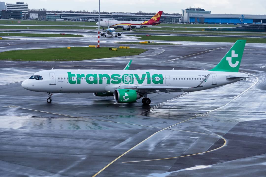 Transavia Airbus aircraft taxiing on a wet airport runway with a vibrant green branding.