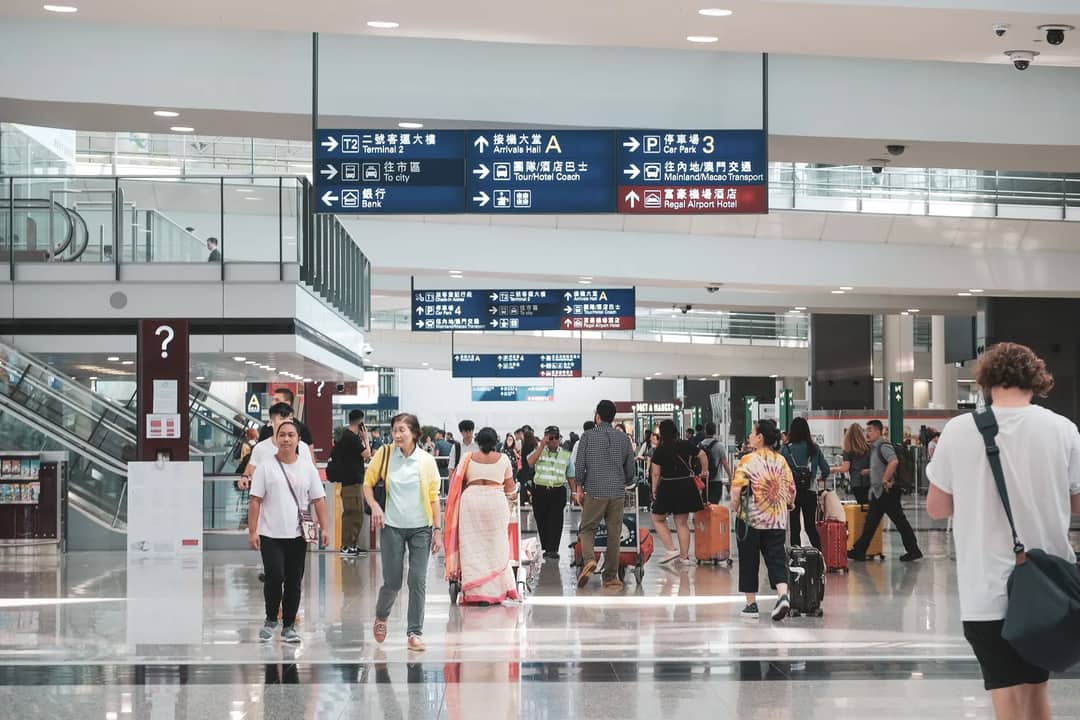 Crowded Hong Kong airport terminal with diverse passengers and informative signage.