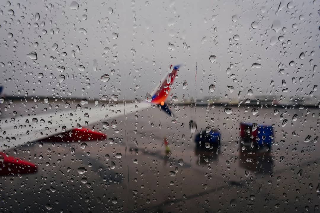 Raindrops on a window with an airplane in the background at an airport, creating a moody travel scene.
