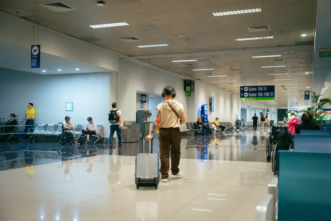Passengers in a spacious airport terminal, some seated and others walking.