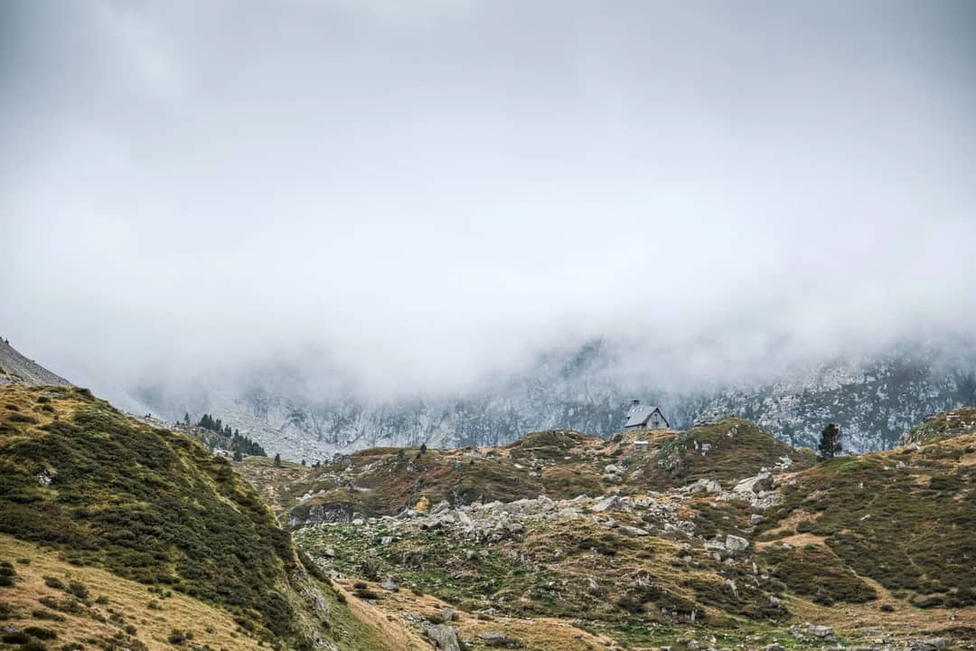 Misty mountain landscape in the Pyrenees, featuring a remote refuge under cloudy skies.