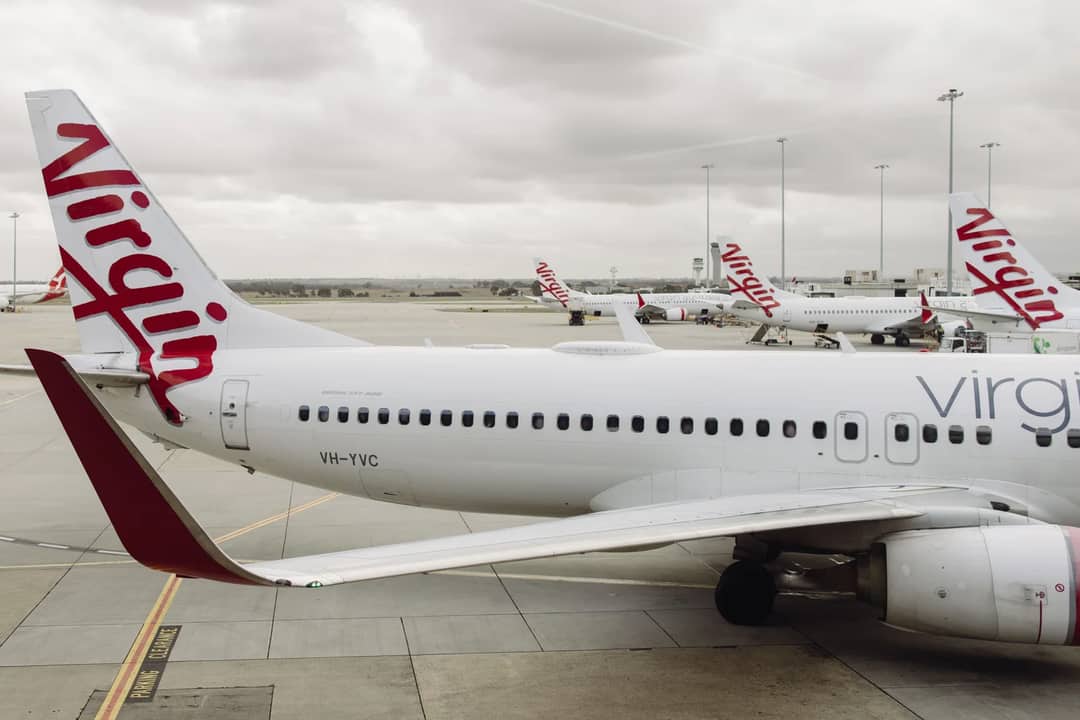 Virgin Australia Boeing 737 aircraft parked at Melbourne Airport under cloudy skies.