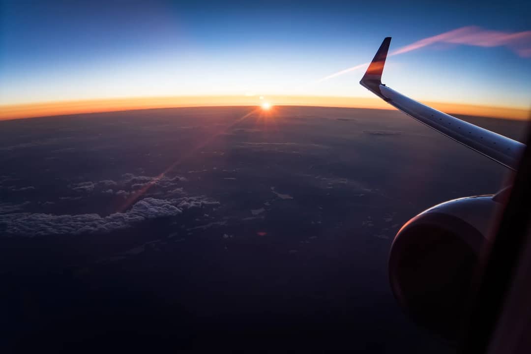 Stunning aerial view from an airplane window showing the wing and a sunset over the clouds.