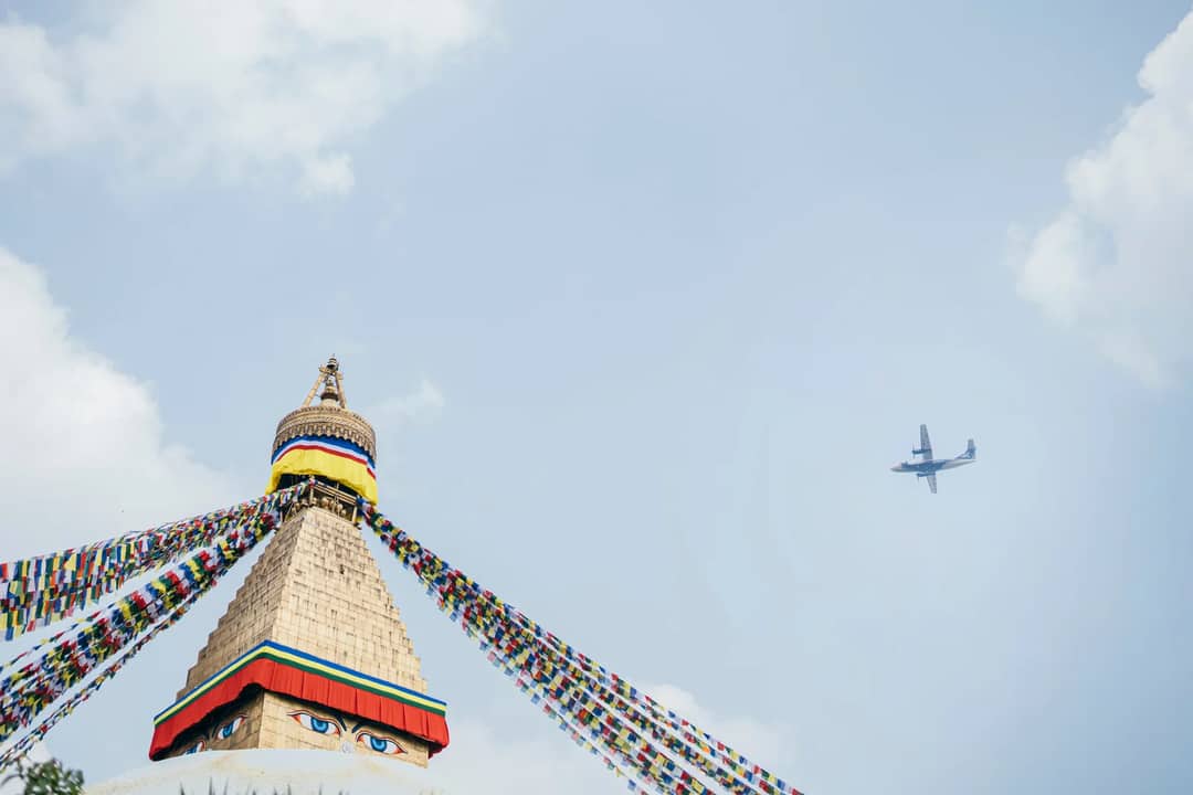 Boudhanath Stupa in Kathmandu, Nepal with vibrant prayer flags and an airplane in the sky.