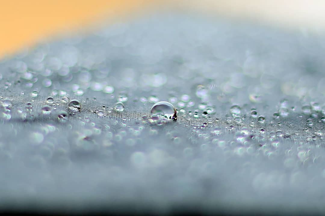 Water beading on the surface of a technical fabric — the repellent finish that makes rain roll off is a surface treatment, not the membrane