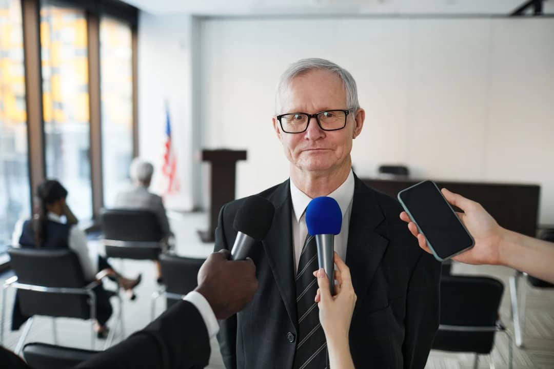 Senior man in formal attire being interviewed in a conference room.