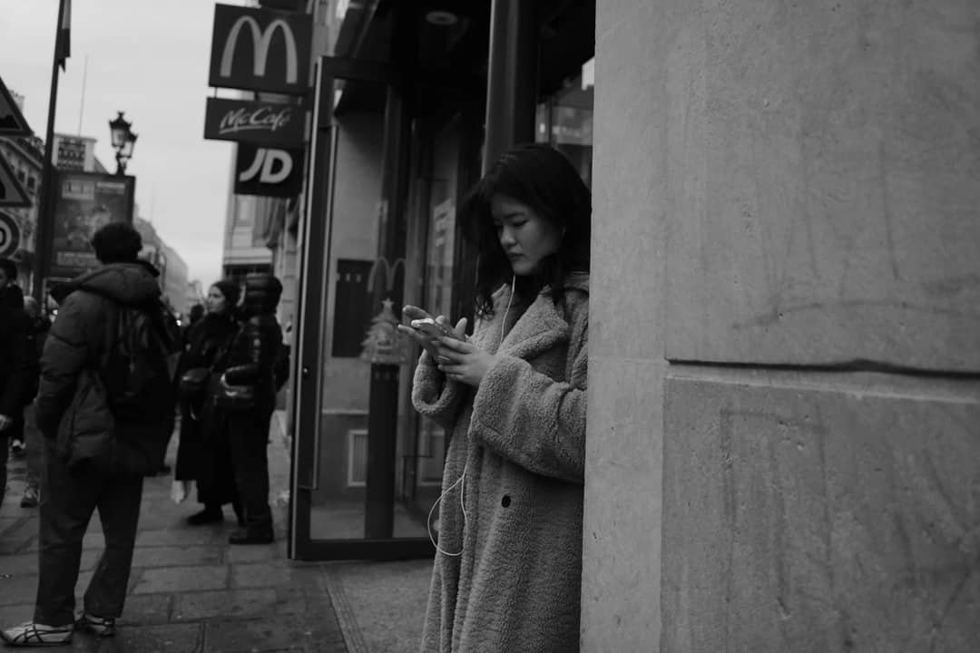Black and white city scene with a young woman using smartphone outside McDonald's.