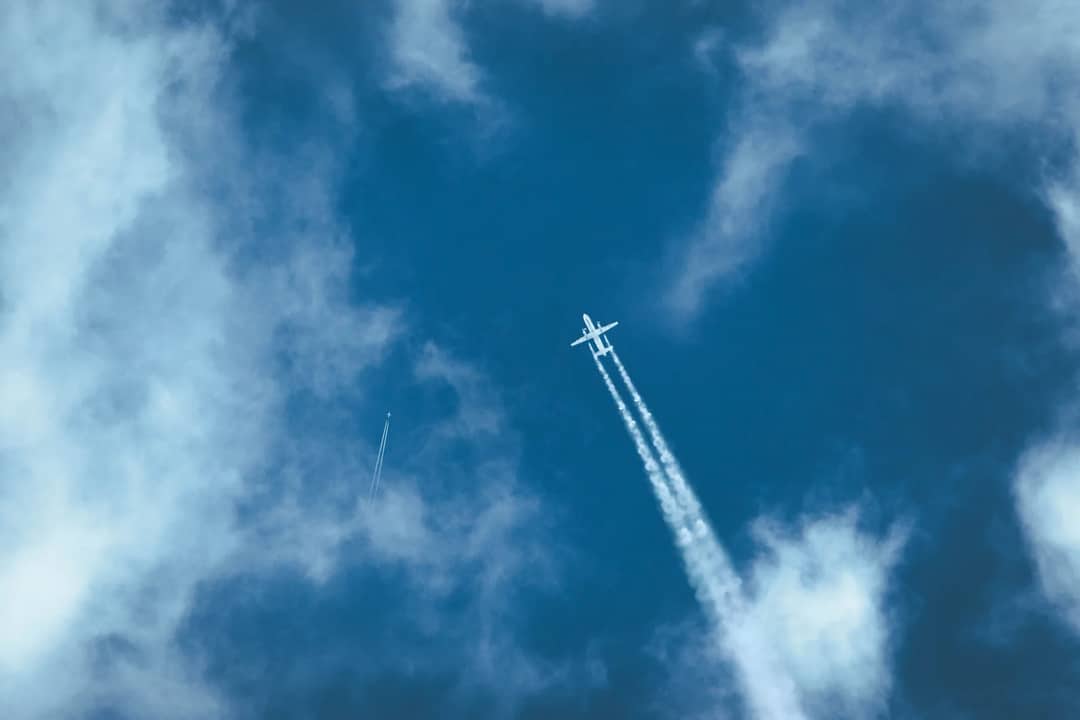 Airplane flying through a clear blue sky leaving a long contrail behind.