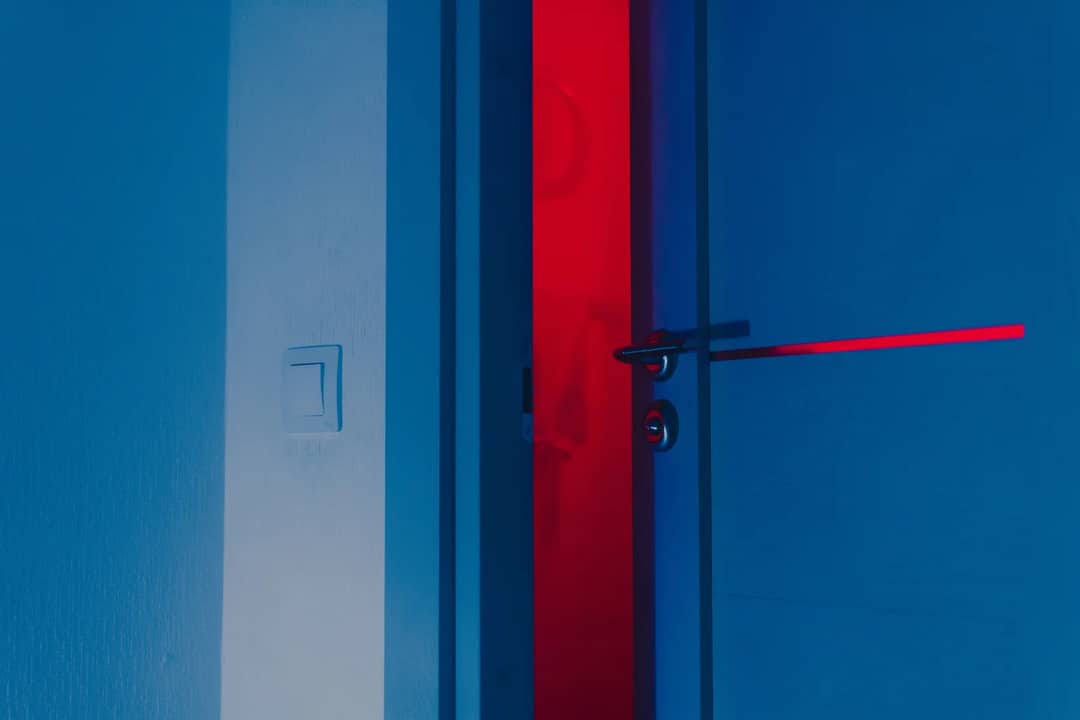 A half-open blue door illuminated by a dramatic red light reveals a unique interior atmosphere.
