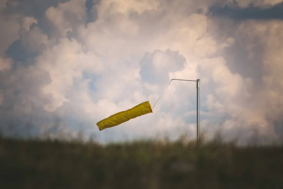 A yellow windsock billowing in the wind set against a dramatic cloudy sky in the countryside.