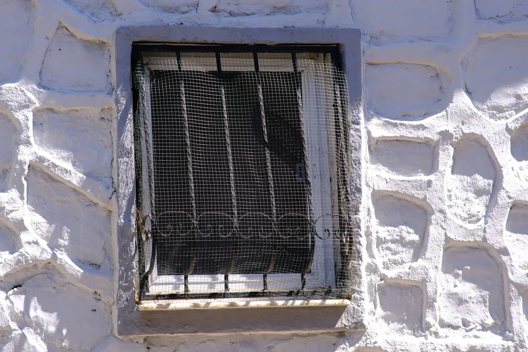 Close-up of a rustic window with an iron grate in a textured white wall in Foça, İzmir, Türkiye.
