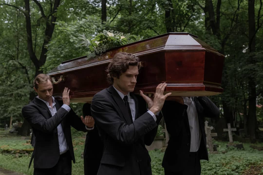 Men solemnly carrying a coffin through a cemetery, symbolizing loss and mourning.